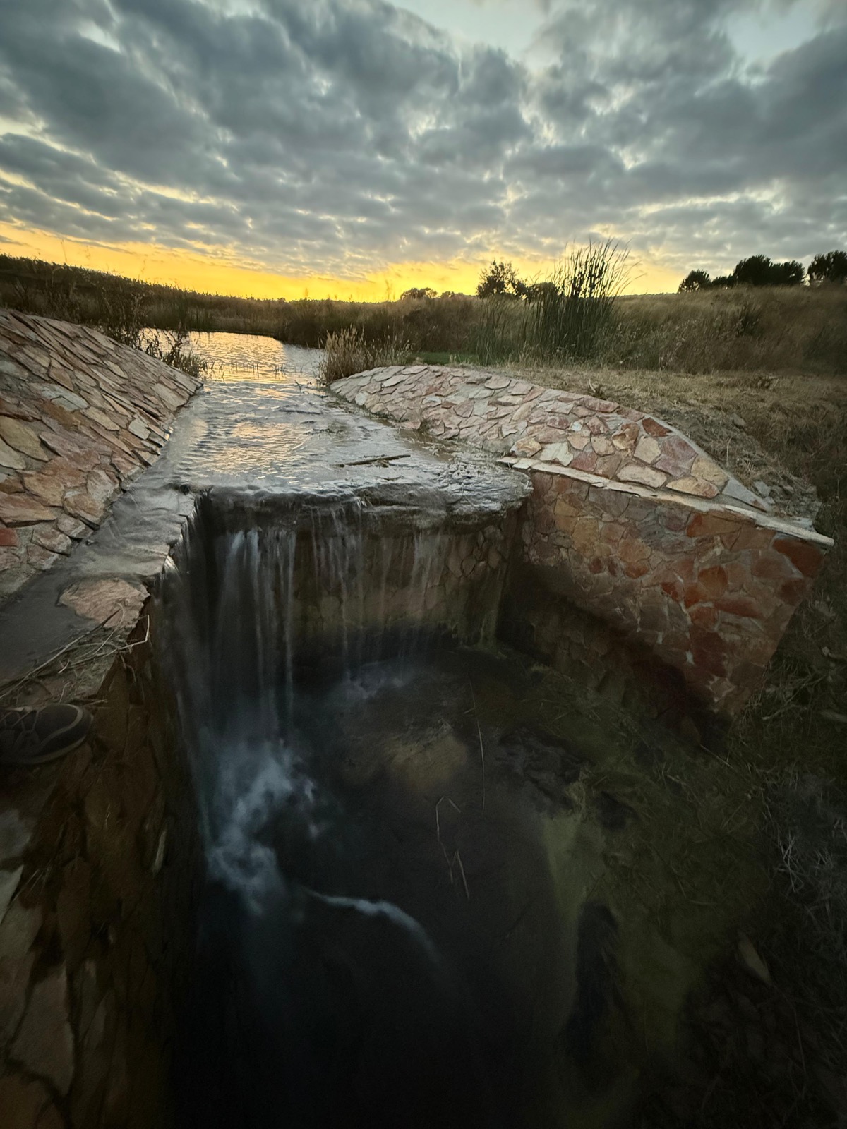 Stone waterfall and pond at sunset